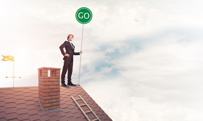 Businessman in suit on house top with ecology concept signboard. Mixed media