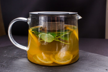 hot tea with mint and lemon in a glass pot on  black background
