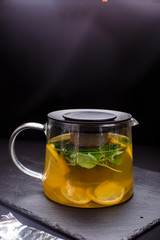 hot tea with mint and lemon in a glass pot on  black background