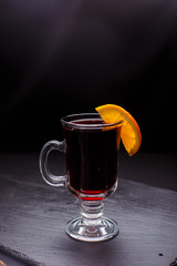 Mulled wine with cinnamon in the transparent glass on the black background