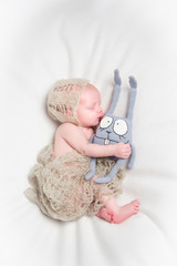 Newborn baby sleeps hugging knitted rabbit on a white blanket