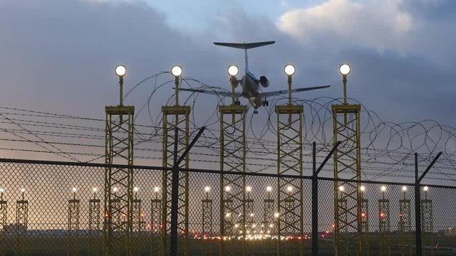 Airplane landing on illuminated runway in early evening, slow motion.