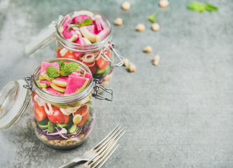 Healthy take-away lunch jars. Vegetable and chickpea sprout layered vegan salad in glass jars, grey...