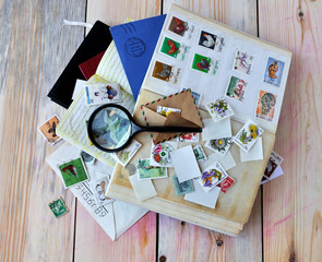 Magnifying glass, postage stamps and envelopes on wooden background.