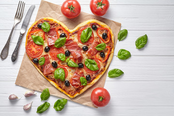 Heart shaped prosciutto pizza tasty love concept Valentine's Day design symbol romantic restaurant dinner Italian food. Olives, tomatoes, basil and mozzarella cheese meal served on white background