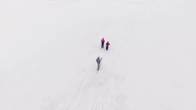 Camera flying back of Caucasian family running on skies on the ice of lake at winter. Top view