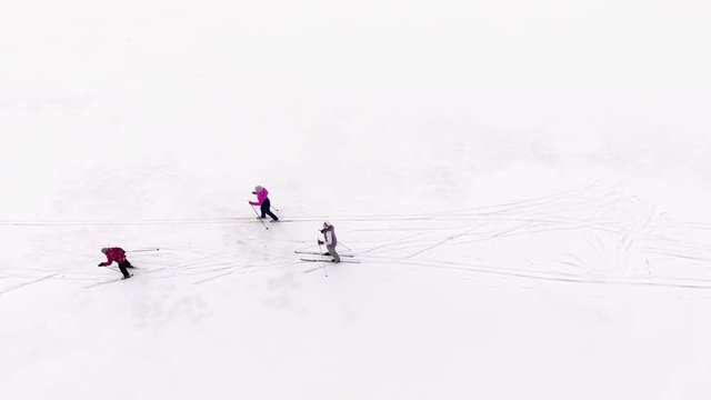 Three skiers ride on cross-country ski on a snowy spacious field, top view