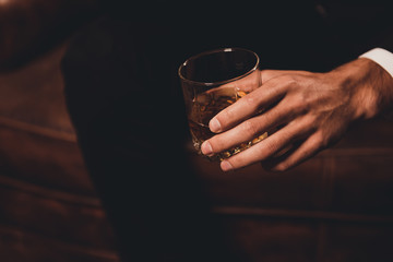 Close up of man's hand holding class of whiskey