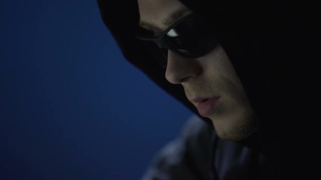 Closeup of man in sunglasses committing crime, illegally using company computer