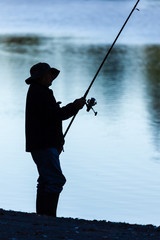 Fisherman silhouette with fishing rod and water.