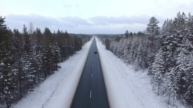 Camera flight along winter road in evergreen forests of Karelia. Police car driving on highway. Front view from flying drone. Kola route to the Murmansk; north of Russia
