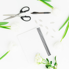 Home office workspace with notebook, clips, pen, scissors and flowers. Flat lay, top view