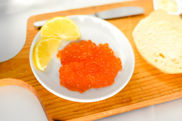 Red caviar, lemon and bread on wooden board white table background