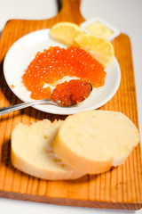 Red caviar, lemon and bread on wooden board white table background