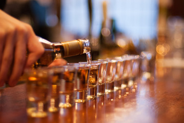 Close-up of a bartender pouring alcohol into a line of shot glasses on a bar counter