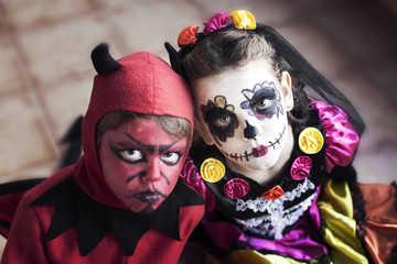 Boy dressed as the devil  for Halloween and girl dressed as La Catrina (Calavera Catrina) for Dia de muertos (Day of the Dead) with sugar skull make-up
