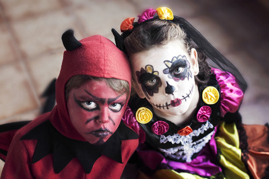 Boy dressed as the devil  for Halloween and girl dressed as La Catrina (Calavera Catrina) for Dia de muertos (Day of the Dead) with sugar skull make-up