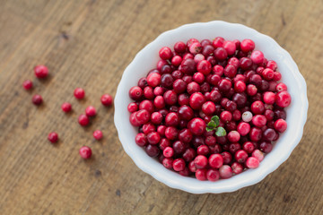 Wild and ripe cranberry in white plate on brown wooden background