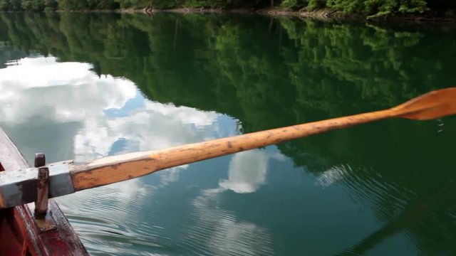 Rowing boat trip on the calm Biorgadskoe lake. Wooden oar pull green water. Nature of the Biogradska Gora national park. Montenegro
