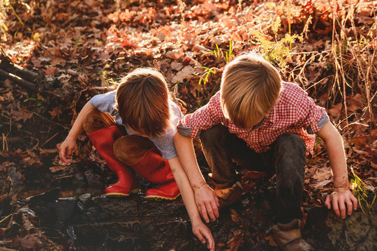 Close-up of two young boys crouching side by side next to a river  playing on an autumn day