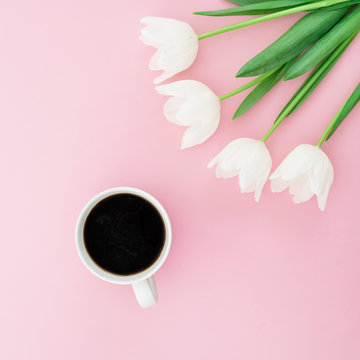Black coffee mug and white tulip, roses flowers bouquet on pink background. Flat lay, top view. Woman morning