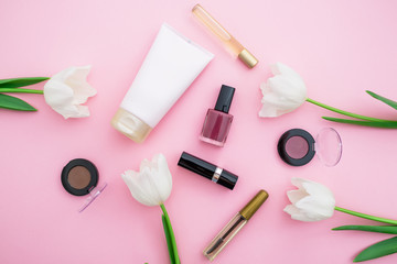 Obraz na płótnie Canvas Flat lay, top view, feminine desk workspace with cosmetics, lipstick tulips on pink background.