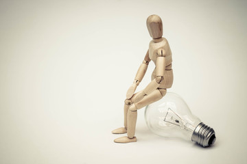 Wood Figure Mannequin sit on incandescent light bulb and think  