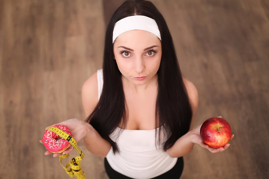 Beautiful young woman making choice between apple and donut on wood background