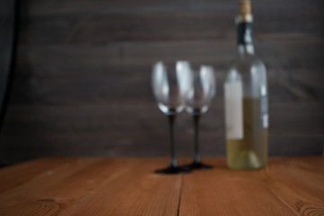 blurred image with two wine glasses and bottle of white wine. wooden background. selective focus. out of focus image