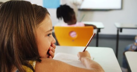 Schoolgirl whispering into her friends ear in classroom - Powered by Adobe