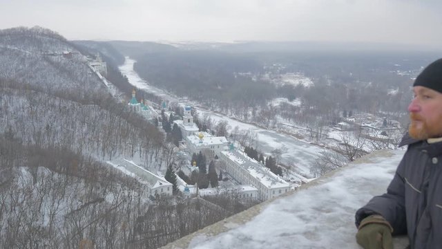 a Grand View on Sviatogorskaya Lavra, Located in Mountains, Covered With Fir Trees and Deep Snow, and a Man Looking at it From Artyom Monument Deck