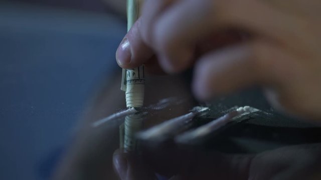 Person inhaling cocaine line through rolled banknote, drug addiction problem