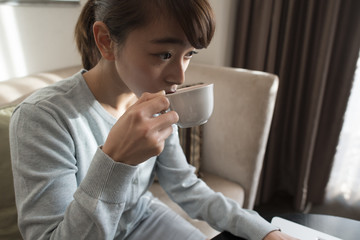 A young woman is sitting on a sofa and drinking coffee