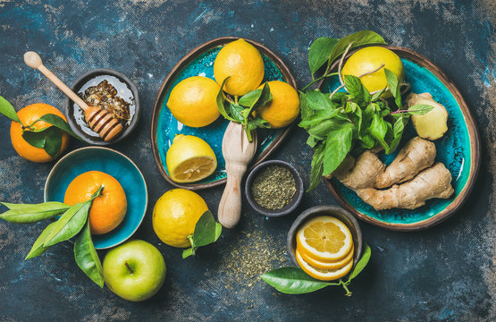 Ingredients for making natural hot drink in blue ceramic plates over dark blue shabby background, top view. Oranges, mint, lemon, ginger, honey and apple. Clean eating, detox, dieting concept