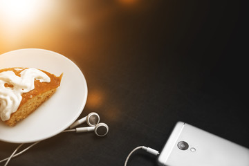 Smartphone with headphones and cake on a black background