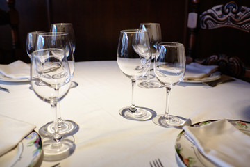 Empty glasses in a restaurant on white tablecloth. Shade, brown background and carved chairs.