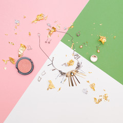 Creative flat lay of girly accessories such as necklace and earrings on pink and green and white background, top view