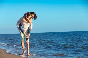 Handsome man giving piggy back to his girlfriend at the beach