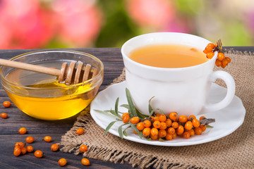 Tea of sea-buckthorn berries with honey on wooden table blurred garden background