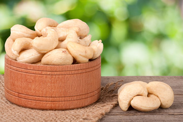 cashew nuts in a wooden bowl on the board with blurred garden background