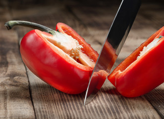 Big kitchen knife cut a bell pepper on wooden table