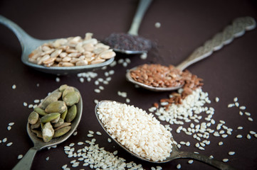 Obraz na płótnie Canvas Variety of seeds in spoons over dark background
