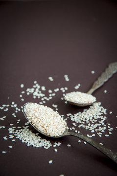 Sesame seeds in spoons over dark background