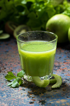 glass of juice of celery and greens on blue background, vertical