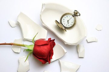 Red Rose and pocket watch laying on a broken bowl