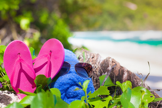 pink flip flops, sunglasses and blue towel on a tropical Seychelles beach. Mahe island