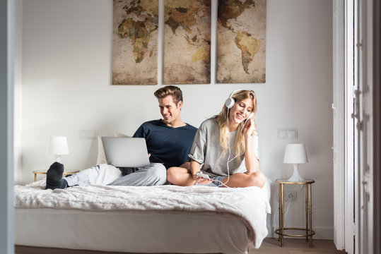 couple on bed entertained on the computer and listen to music