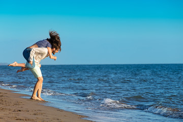 Handsome man giving piggy back to his girlfriend at the beach