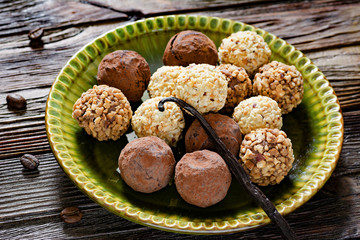 Vegetarian truffle balls with dates, nuts, dried fruits, vanilla and cocoa powder on green plate over wooden background. Concept of vegan sweets, healthy eating, dieting. Closeup view