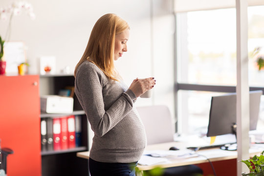 pregnant businesswoman with cup of tea at office